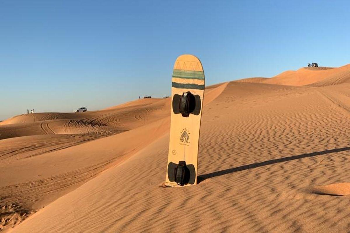 Sandboard planted in Dubai red sand dunes with safari vehicles in the distance