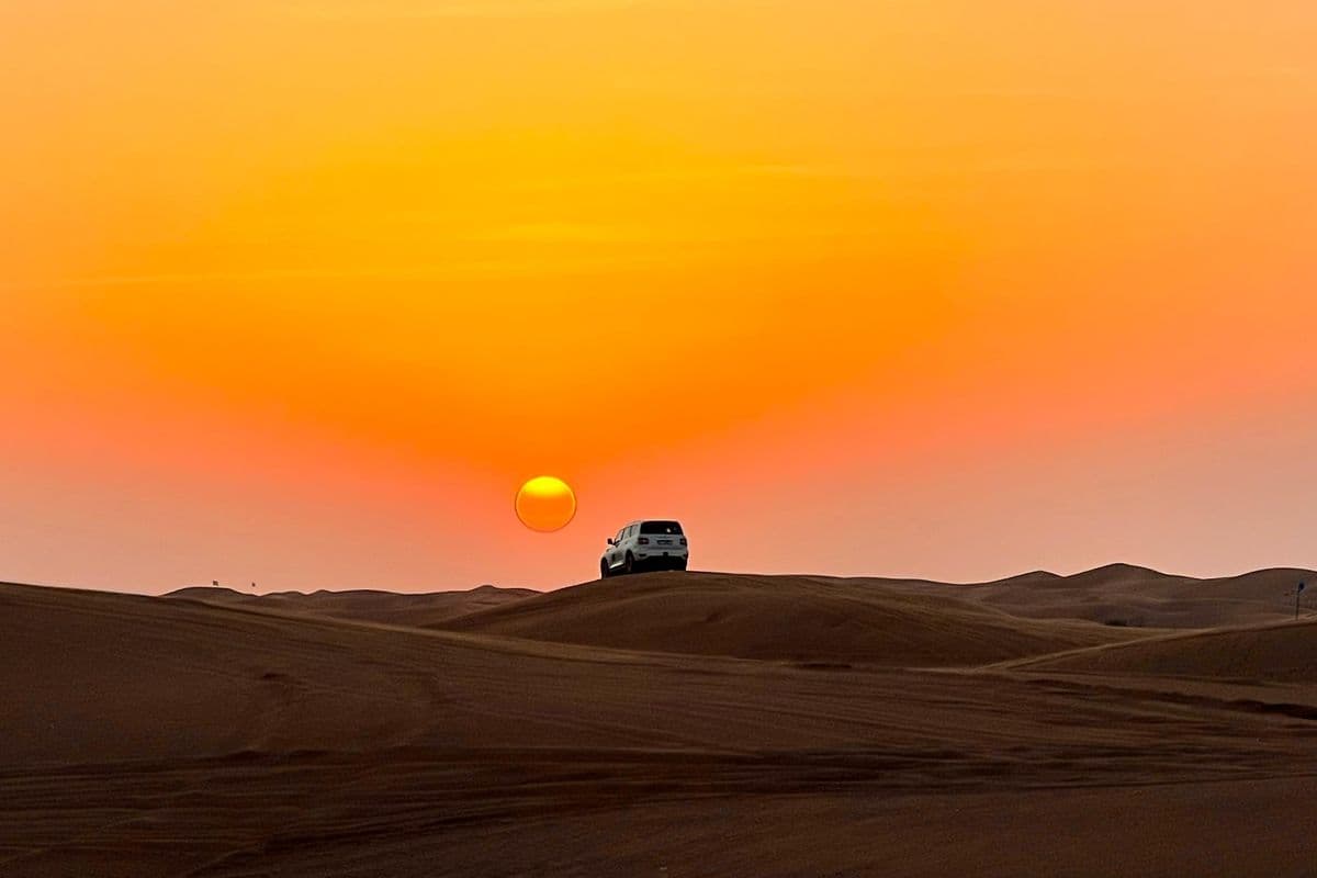 Land Cruiser on Dubai desert dune ridge at sunrise with orange sky