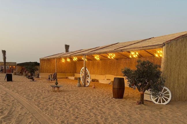 Reed huts and a wagon-wheel decoration at the Lahbab desert camp at dusk