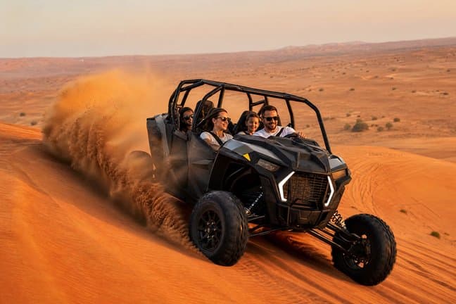 Family self-driving a 4-seater dune buggy across Dubai red dunes at golden hour