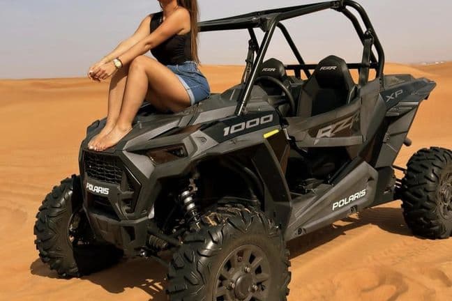 Woman sitting on gray Polaris RZR XP 1000 dune buggy in Dubai desert sand dunes