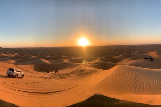 Panoramic sunset view of Dubai desert with Land Cruiser, quad bikes and buggies on golden sand dunes