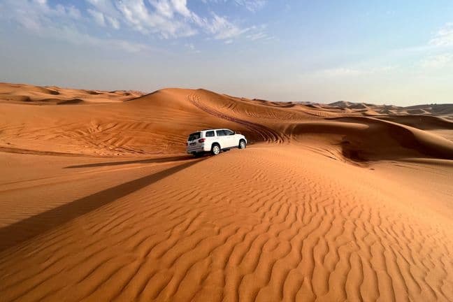 White Toyota Land Cruiser on rippled golden sand dunes under blue sky with wispy clouds in Dubai desert
