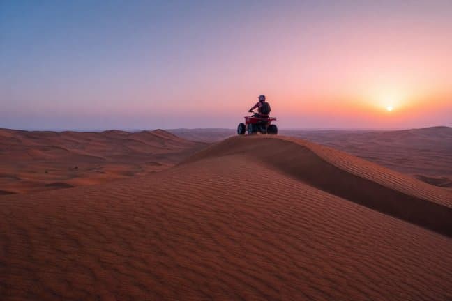 Quad bike rider on an empty Dubai desert dune ridge at sunrise