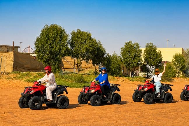 Group of guests on red quad bikes with helmets at a Dubai desert safari camp