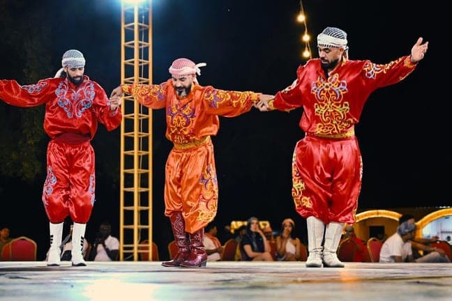 Three folk dancers in red outfits on stage at the desert camp
