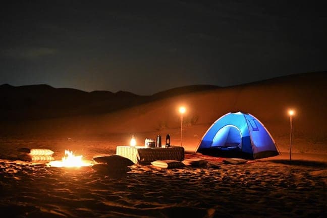 Lit tent and campfire on the dunes during an overnight desert safari