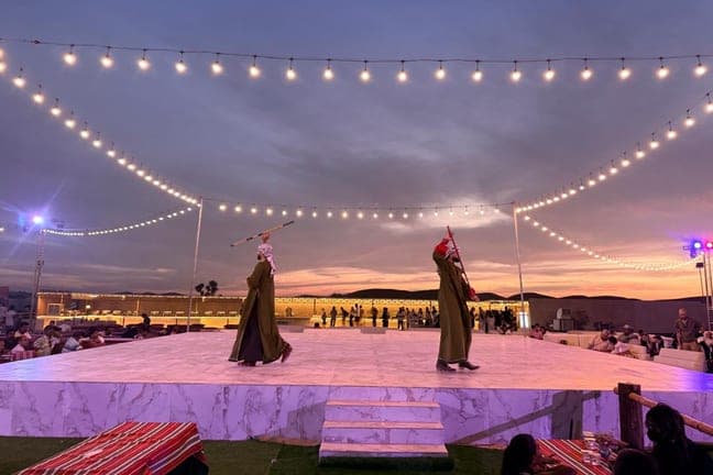 Desert camp stage under string lights at sunset during the evening show