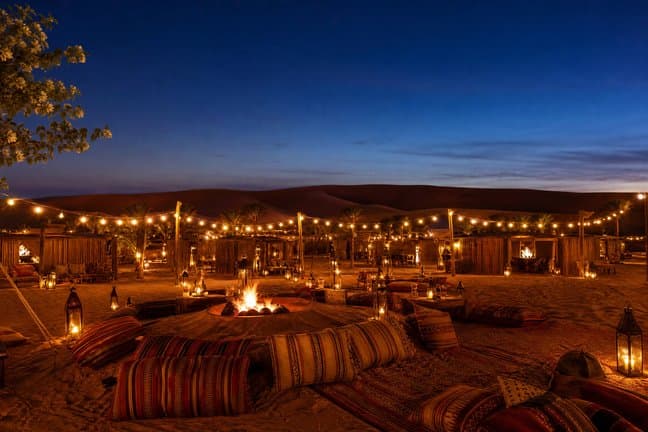 Dubai desert safari camp lit with lanterns and a fire pit at blue hour