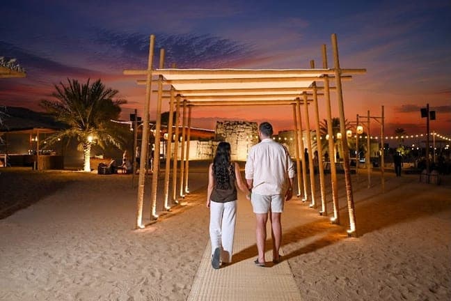 Couple walking into the desert camp under a lit pergola at dusk