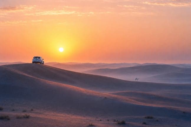 Toyota Land Cruiser on red sand dune at Dubai desert sunrise with soft pink and orange sky