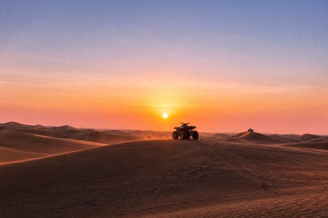 ATV quad bike on red sand dune ridge at Dubai desert sunrise with pink and orange sky