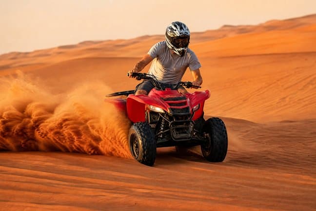 Rider in a helmet spraying sand on a quad bike across Dubai's red desert dunes