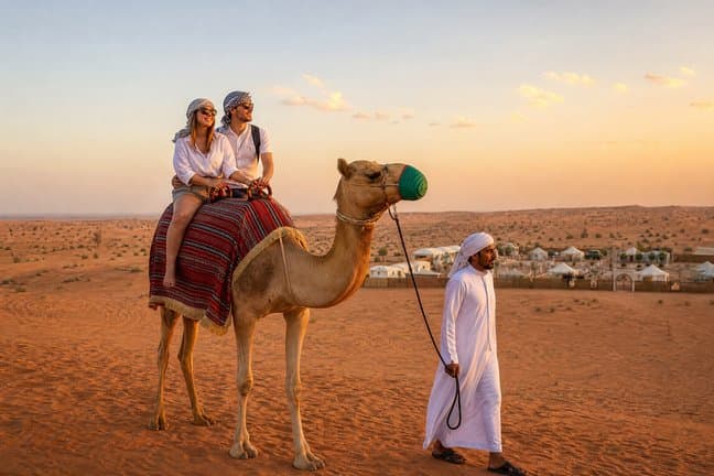 Couple on a camel led by a handler at a Dubai desert safari camp at sunset