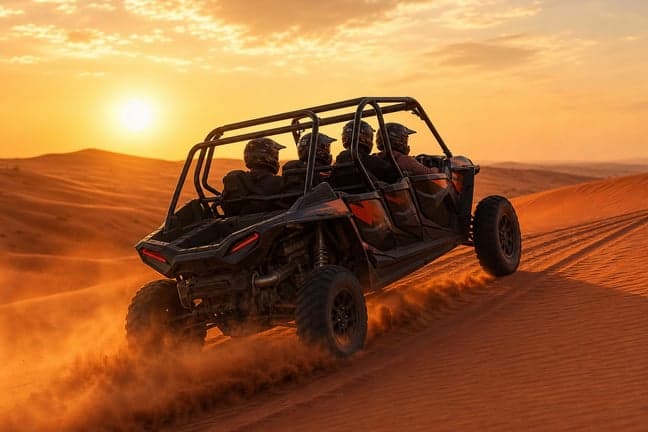Red Polaris RZR 4-seater dune buggy with family driving on red sand dune at golden hour