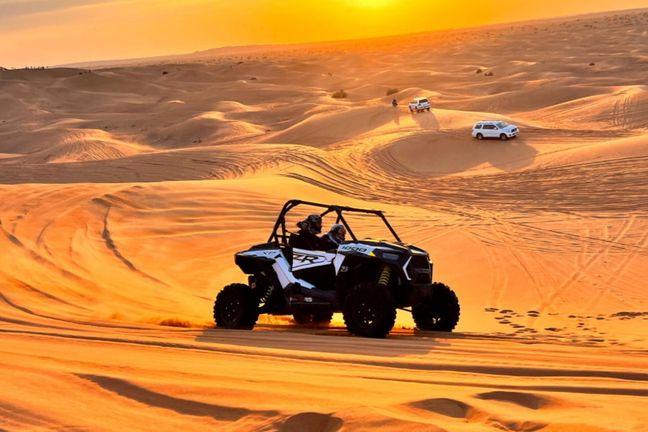 Polaris RZR dune buggy racing across Dubai desert dunes at sunset with escort vehicle