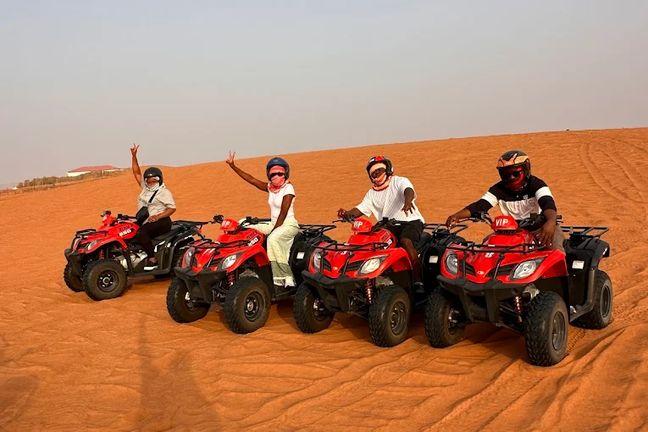Group of four tourists with helmets on red quad bikes on Dubai desert dunes