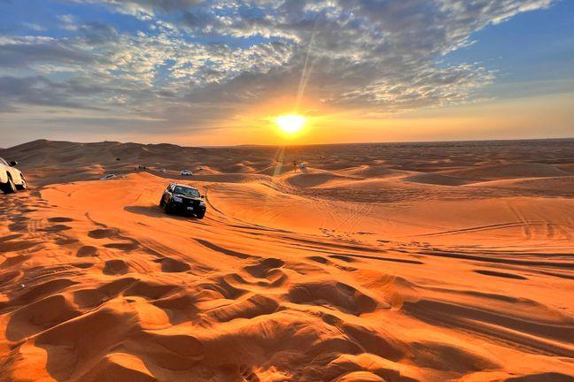 4x4 vehicle on golden Dubai desert dunes at sunset with dramatic sun rays piercing through clouds