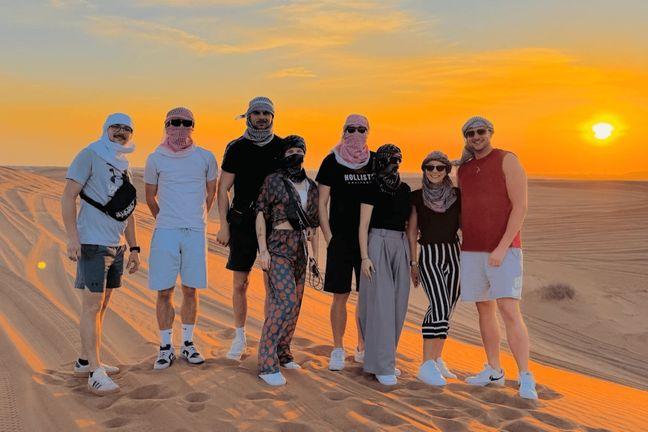 Group of tourists wearing keffiyeh posing on Dubai red sand dunes at sunset