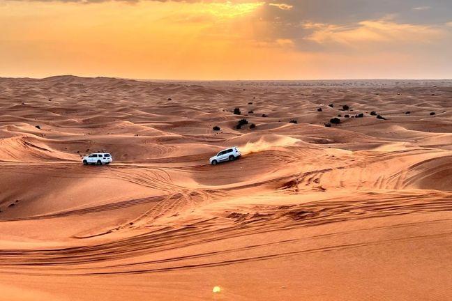 Two Land Cruisers dune bashing on Dubai desert sand at golden hour
