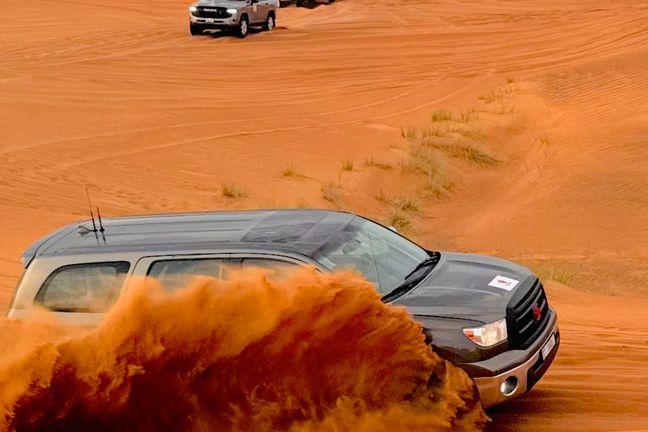 Close-up action shot of Toyota Tundra creating massive orange sand spray during Dubai dune bashing adventure