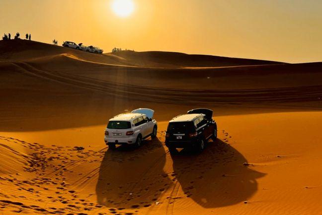 Two Land Cruisers parked between Dubai desert dunes with tourists watching sunset