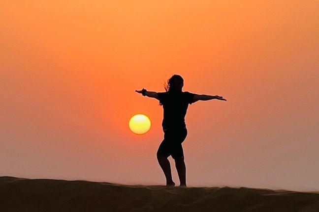 Tourist silhouette with arms spread on Dubai desert dune at sunset
