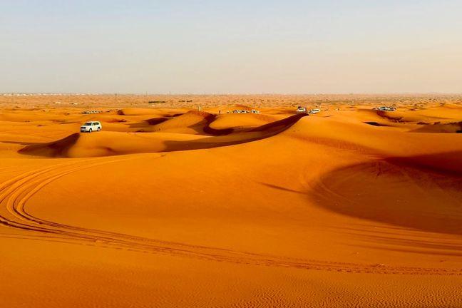 Safari 4x4 vehicles crossing vast red sand dunes in Dubai desert at golden hour