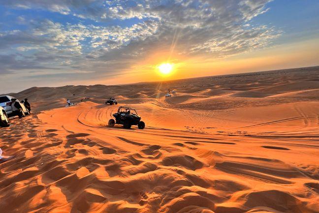 Dune buggies driving across Dubai red sand dunes at golden hour sunset