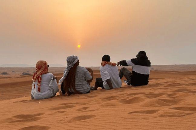 Group of friends sitting on Dubai desert dunes watching sunset during safari