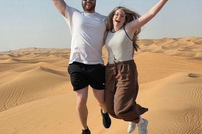 Couple jumping for joy on Dubai desert sand dunes during safari experience