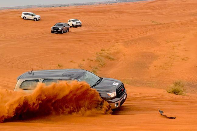 Toyota Tundra dune bashing with dramatic orange sand spray on red Dubai dunes with Land Cruisers in background